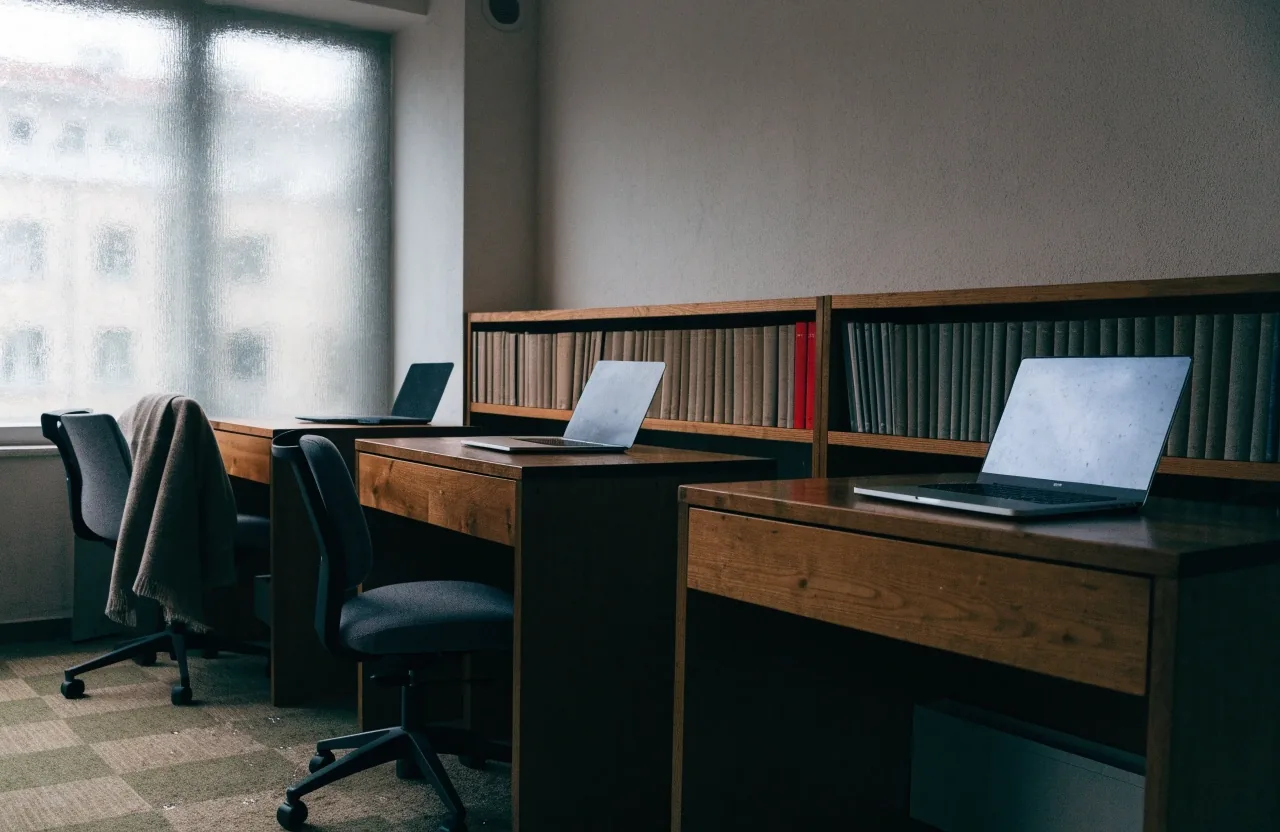 A small Helsinki editorial office with three desks and a shared bookcase in overcast daylight