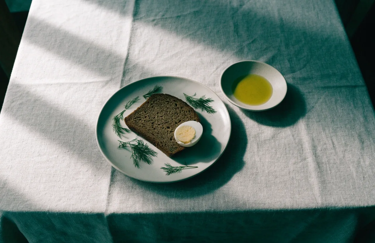 A plate of dark rye bread, boiled egg and fresh greens set on a plain Finnish table